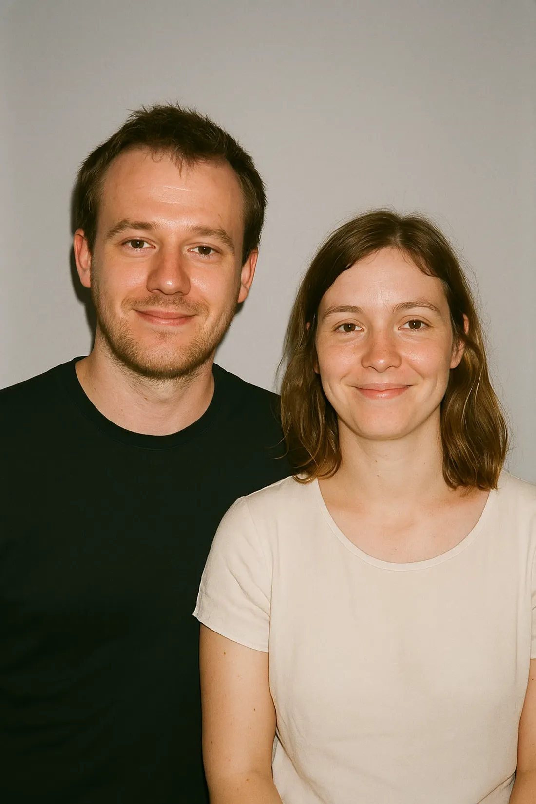 Photo: A couple in a photo booth: flat on-camera light, everyday clothes, plain backdrop